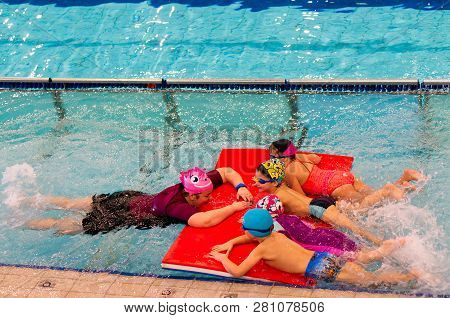 Poznan, Poland - January 26, 2019: Instructor And Three Children Holding On A Mat During Swim Lesson