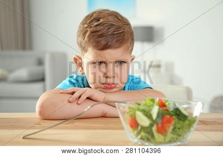 Stroppy Little Boy With Bowl Of Vegetable Salad At Table In Room