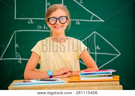Back to school.. Funny beatifull girl sitting in the clasroom against blacboard. Child in school with book and accessories. Education concept