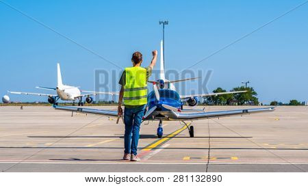 Dispatcher geaturing signs directing the blue shiny sport plane on the airport runway