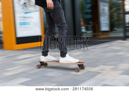 Shot Of Male In Black Jeans And White Sneakers Riding A Longboard In Urban Area, Photo In Motion/ Si