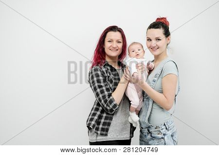 Two Young Women With A Baby On A White Background. Same-sex Marriage And Adoption, Homosexual Lesbia