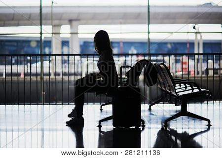 Silhouette Of Young Woman In International Airport Sitting And Waiting For Her Flight.