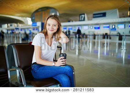 Young Woman In International Airport With Luggage And Coffee To Go, Waiting For Her Flight