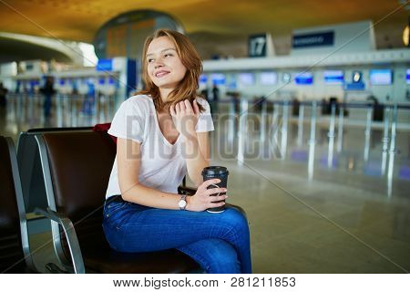 Young Woman In International Airport With Luggage And Coffee To Go, Waiting For Her Flight