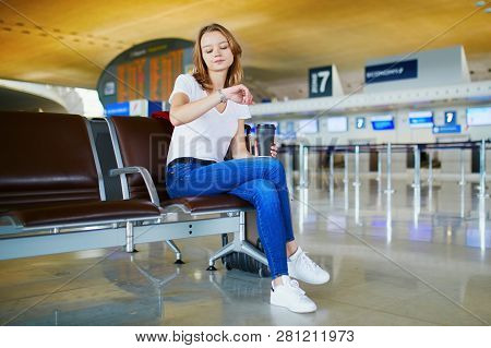 Young Woman In International Airport With Luggage And Coffee To Go, Waiting For Her Flight And Looki