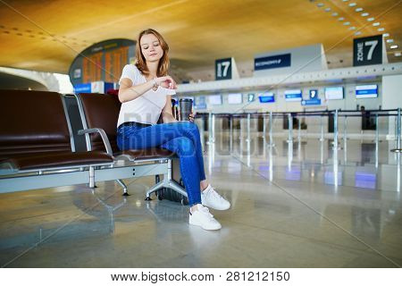 Young Woman In International Airport With Luggage And Coffee To Go, Waiting For Her Flight And Looki