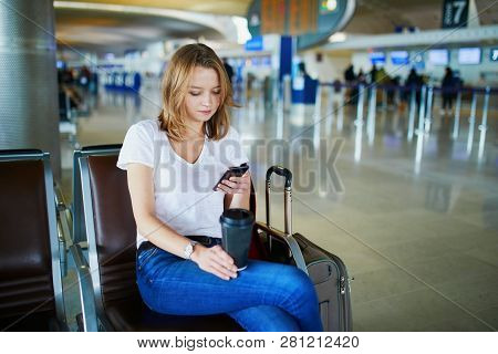 Young Woman In International Airport With Luggage And Coffee To Go, Waiting For Her Flight And Looki