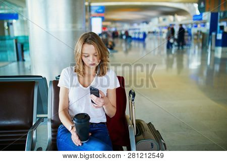 Young Woman In International Airport With Luggage And Coffee To Go, Waiting For Her Flight And Looki
