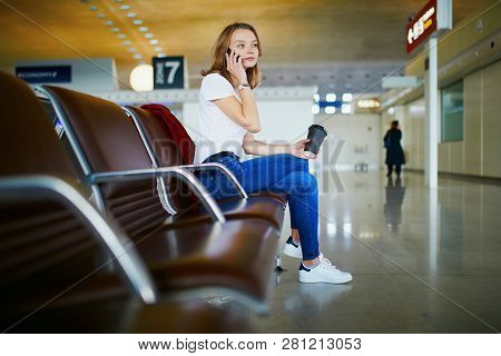 Young Woman In International Airport With Luggage And Coffee To Go, Waiting For Her Flight And Speak