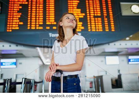 Young Woman In International Airport With Luggage Near Information Board Waiting For Her Flight