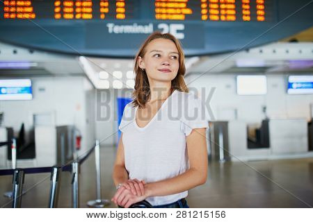 Young Woman In International Airport With Luggage Near Information Board Waiting For Her Flight