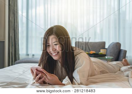 Asian Woman In Bathrope Suit Using The Smart Mobile Phone With Smiling Action On The Bed When Wake U