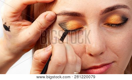 Visagiste With A Brush In One Hand Putting Makeup On The Eyes Of The Model, The Other Hand Pulls The