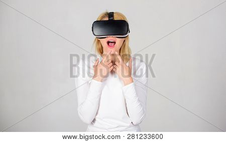 Woman Wearing Virtual Reality Goggles In Grey Background. Amazed Young Woman Touching The Air During
