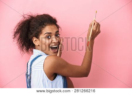 Beautiful young african woman atrist holding a paint brush over pink background