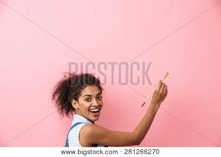 Beautiful young african woman atrist holding a paint brush over pink background