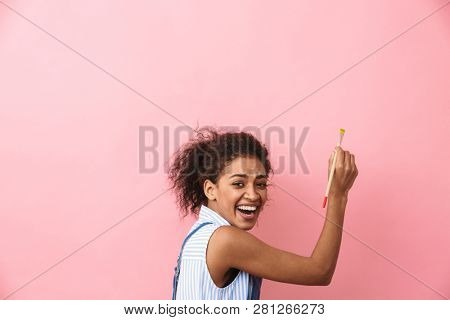 Beautiful young african woman atrist holding a paint brush over pink background
