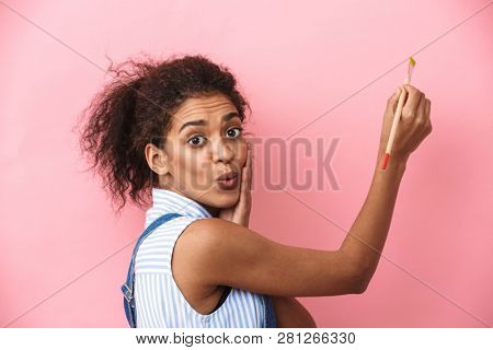 Beautiful young african woman atrist holding a paint brush over pink background