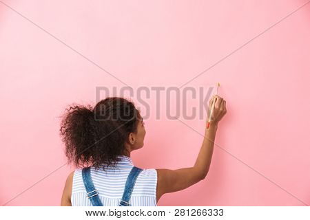 Beautiful young african woman atrist holding a paint brush over pink background