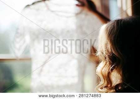 Cropped Shot Of Blonde Woman With Curly Hair Holding And Looking At Beautiful White Wedding Dress On