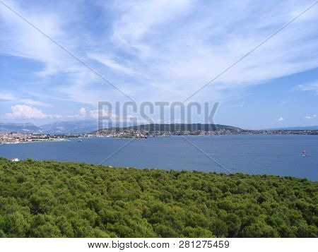 View Of Picturesque Landscape With Blue Sea, Bright Green Foliage And Pinnate Clouds At The Adriatic