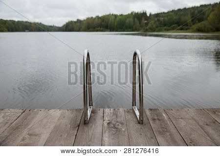 Metal Handrail For Descent Into The Lake, 
Iron Ladder For Swimmers. Wooden Pier On The Lake, Cloudy