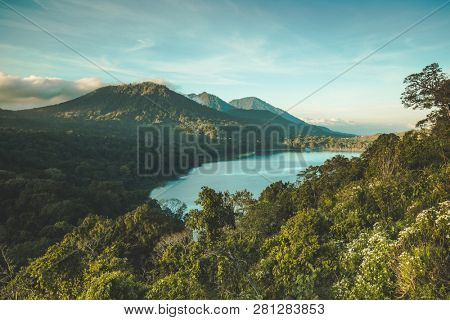 The lake Batur surrounded by the greens and volcano. Bali island, Indonesia. Picturesque overview of the water surface among the dense woods. Popular tourist attraction. Amazing Balinese landscape.