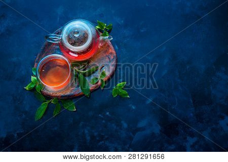 Teapot And Double Wall Glass With Tea Leaves On A Wooden Coaster. Dark Blue Background Flat Lay With