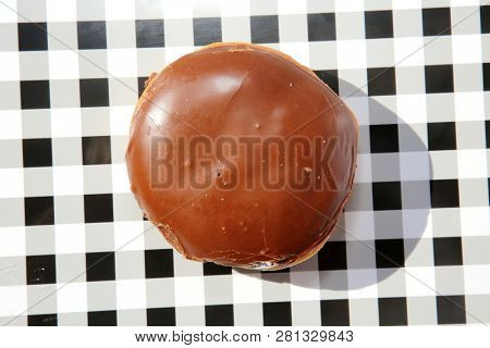 Donut. Donut on a black and white checker tray. Isolated on white. Room for text. Cream Filled Chocolate Covered Donut. Bavarian Cream Filled donut. 

