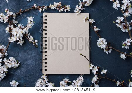 Notepad And Cherry Branches With Spring Flowers On A Dark Blue Background