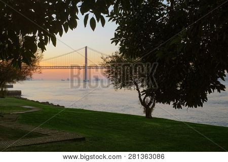 25 April Bridge in Lisbon at sunset seen from a park with trees and grass field
