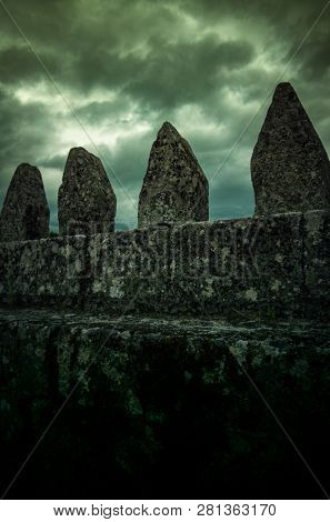 Detail of a  wall with pointy stones against dark cloudy sky