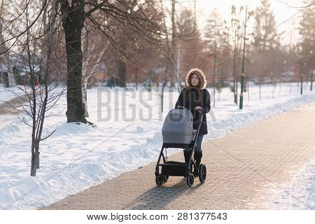 Beautiful Mother Walking In The Park With Her Little Baby In Stoller. Woman Dressed In Blue Jaket Wi