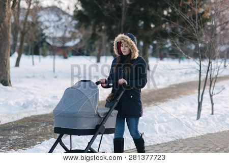 Beautiful Mother Walking In The Park With Her Little Baby In Stoller. Woman Dressed In Blue Jaket Wi