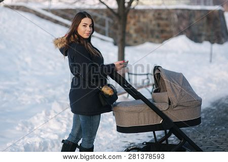 Young Mother Walking With Her Baby In Pram. Beautiful Stoller. Winter Photosession