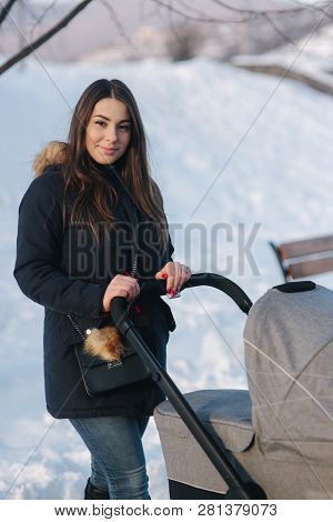 Young Mother Walking With Her Baby In Pram. Beautiful Stoller. Winter Photosession