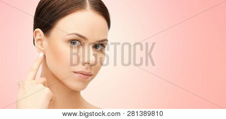 beauty, hearing and plastic surgery concept - face of beautiful young woman pointing finger to earlobe over pink background