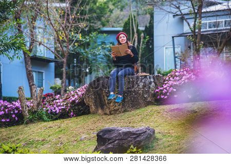 Woman Travel Nature In The Flower Garden. Relax Sitting On Rocks And Reading Books In The Midst Of N