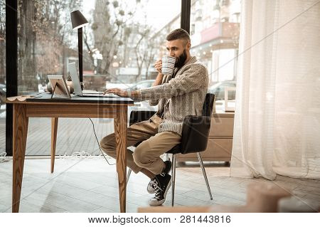 Attentive Good-looking Bearded Man In Knitted Cardigan Sipping Hot Drink