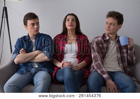 Three Frinds Sitting On Sofa Together. Teenage Girl Sitting On Couch Between Two Of Her Guy Frinds W