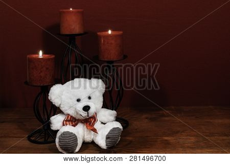 Three Red Candles In Metal Holoders And Red Rose, One Teddy Bear On Wooden Table.