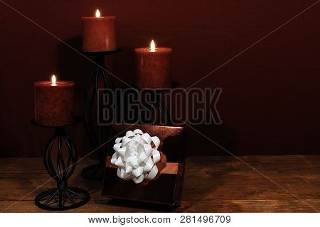 Three Red Candles In Metal Holoders And Red Rose, Present With White Bow On Wooden Table.