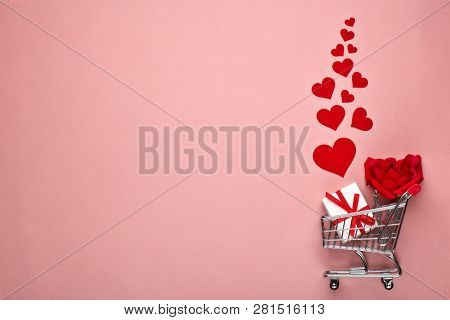 Shopping trolley, gift box, flower and decorative red hearts on pink background with copy space. Valentine's day, Mother's day,  wedding