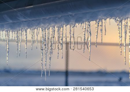 Transluscent Icicles On Roof Against Fence And Sky