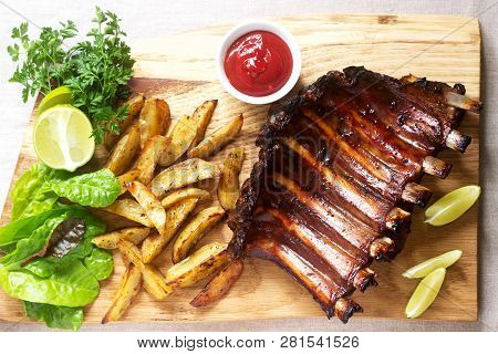 Homemade Baked Meat Ribs Served With French Fries, Herbs, Lime And Ketchup On A Wooden Board. Rustic