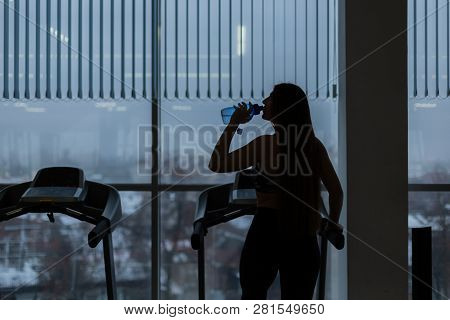 Gym Woman Working Out Drinking Water Smiling Happy Standing By Moonwalker Fitness Machines. Beautifu