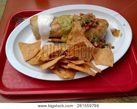 Chimichanga With Guacamole,and Salsa On Top.  On A Plate, On Top A Table.  Taken At A Local Fast Foo