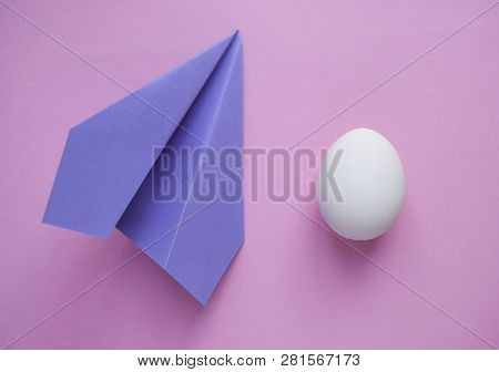 A White Single Egg On Pink Background With Paper Plane And Copyspace. Minimalistic Concept.