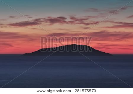Small Island Silhouette In The Middle Of The Sea At Sunrise, Colorful Sky With Red, Cyan And Blue To